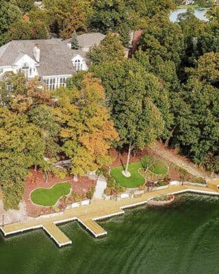 Aerial view of a luxury lakeside home surrounded by vibrant trees and a wooden dock.