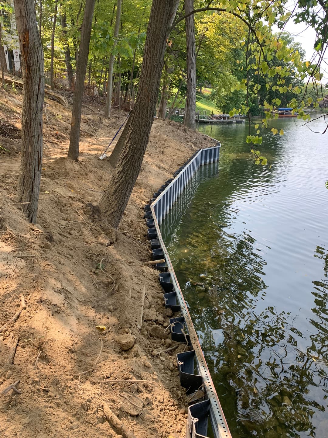 Seawall along a lake, lined with trees and sandy bank, reflecting nature's tranquility.