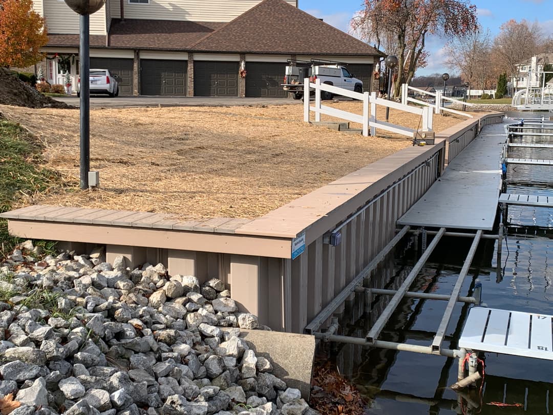Dock edge with wooden decking and gravel, by a marina and residential area in autumn.
