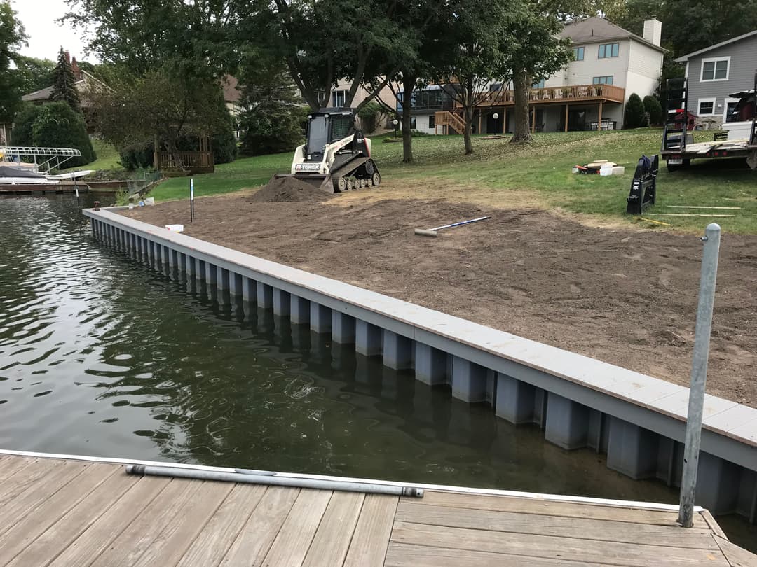 Construction of a shoreline dock with machinery and freshly leveled sand on a lakefront property.