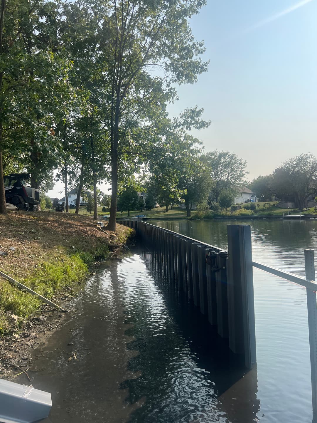 View of a serene lake with a shoreline, trees, and a new dock installation along the water's edge.