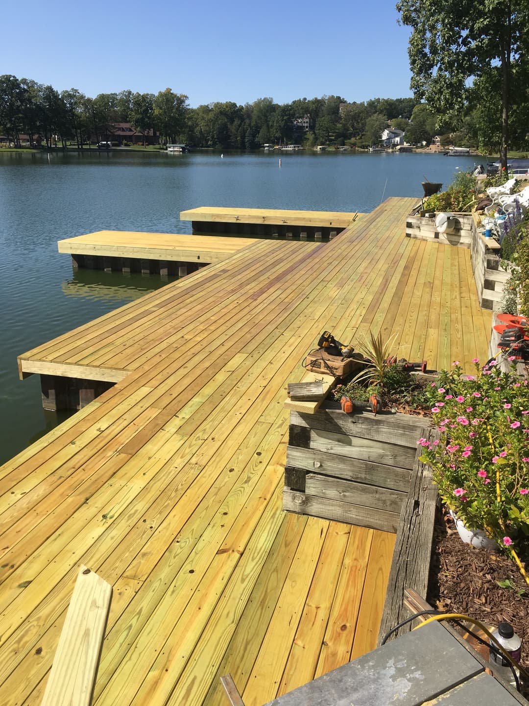 Newly constructed wooden dock with platforms on a lake surrounded by greenery and flowers.