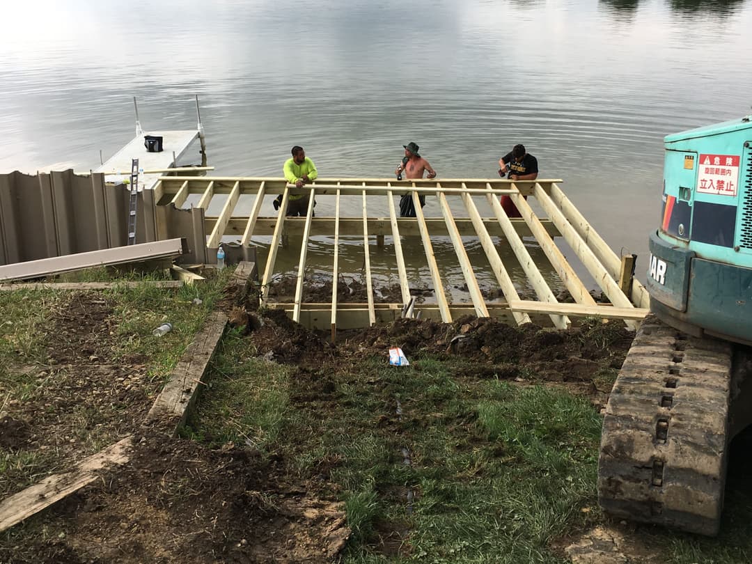 Construction workers building a wooden deck over water with heavy machinery nearby.