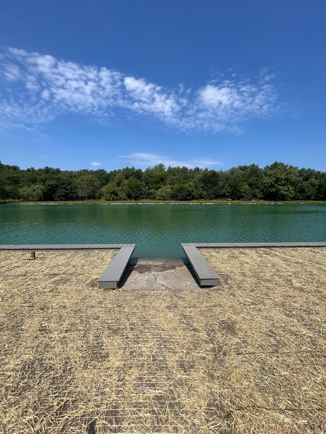Tranquil lake with wooden dock under a clear blue sky and green trees in the background.