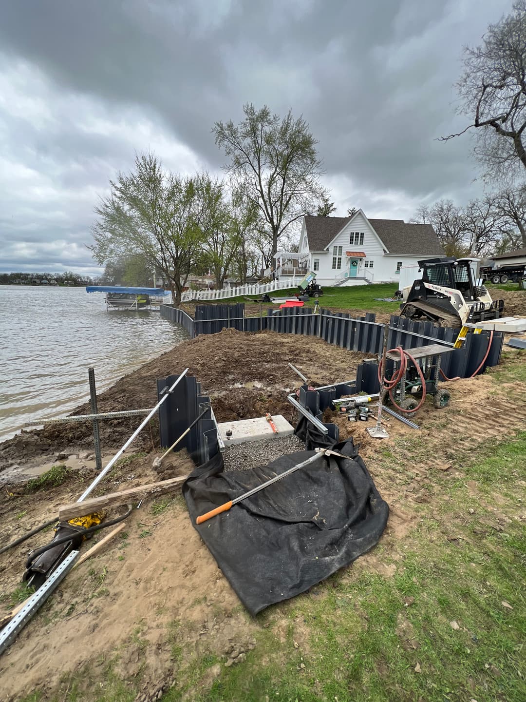 Waterfront property under construction with machinery, landscaping, and a cloudy sky.
