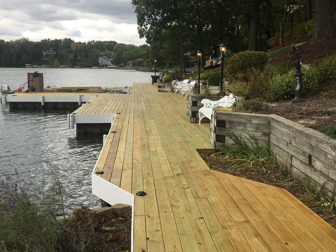 Wooden dock extending into a lake, lined with benches and surrounded by greenery.