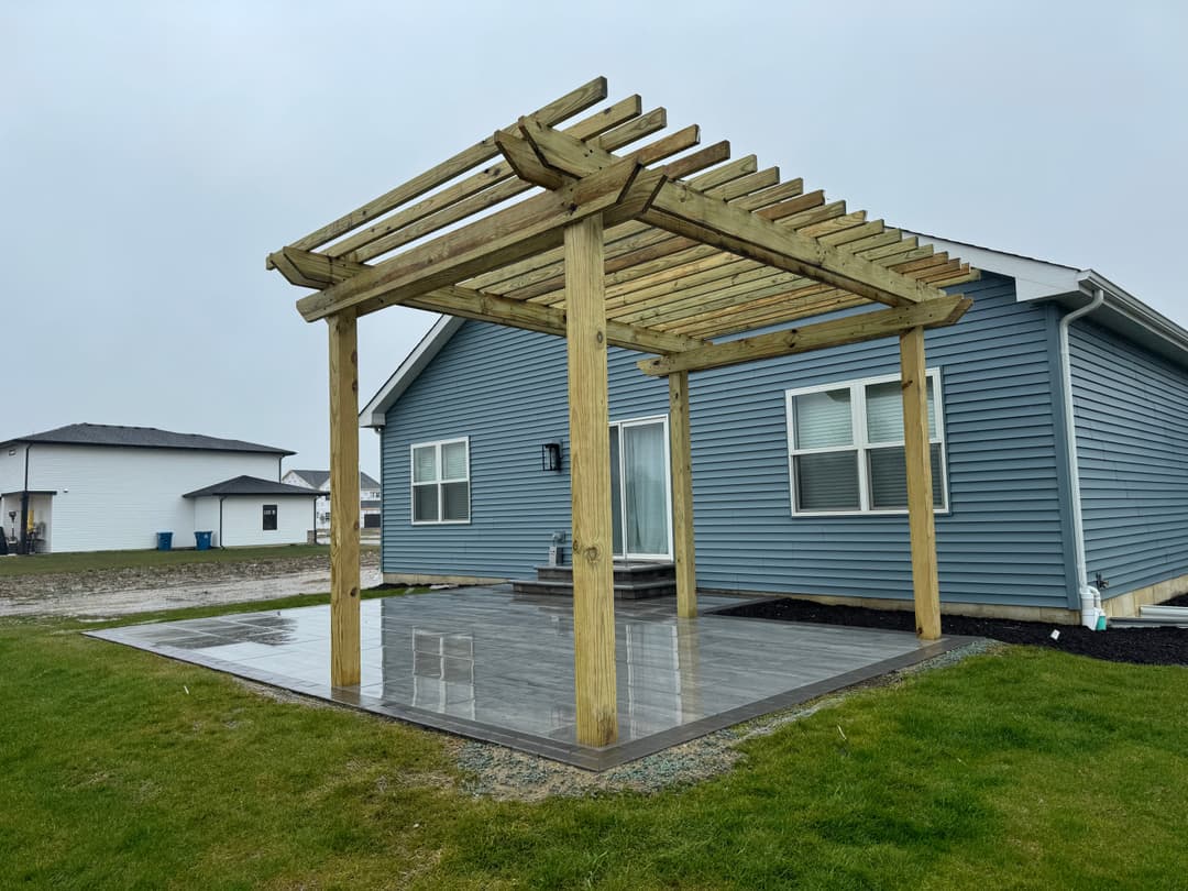 Modern gray house with a wooden pergola and tiled patio on a rainy day. Green lawn in foreground.