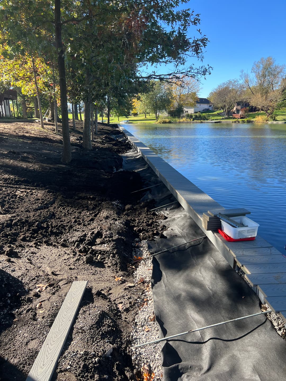 Waterfront property under renovation with dock, trees, and clear blue sky.
