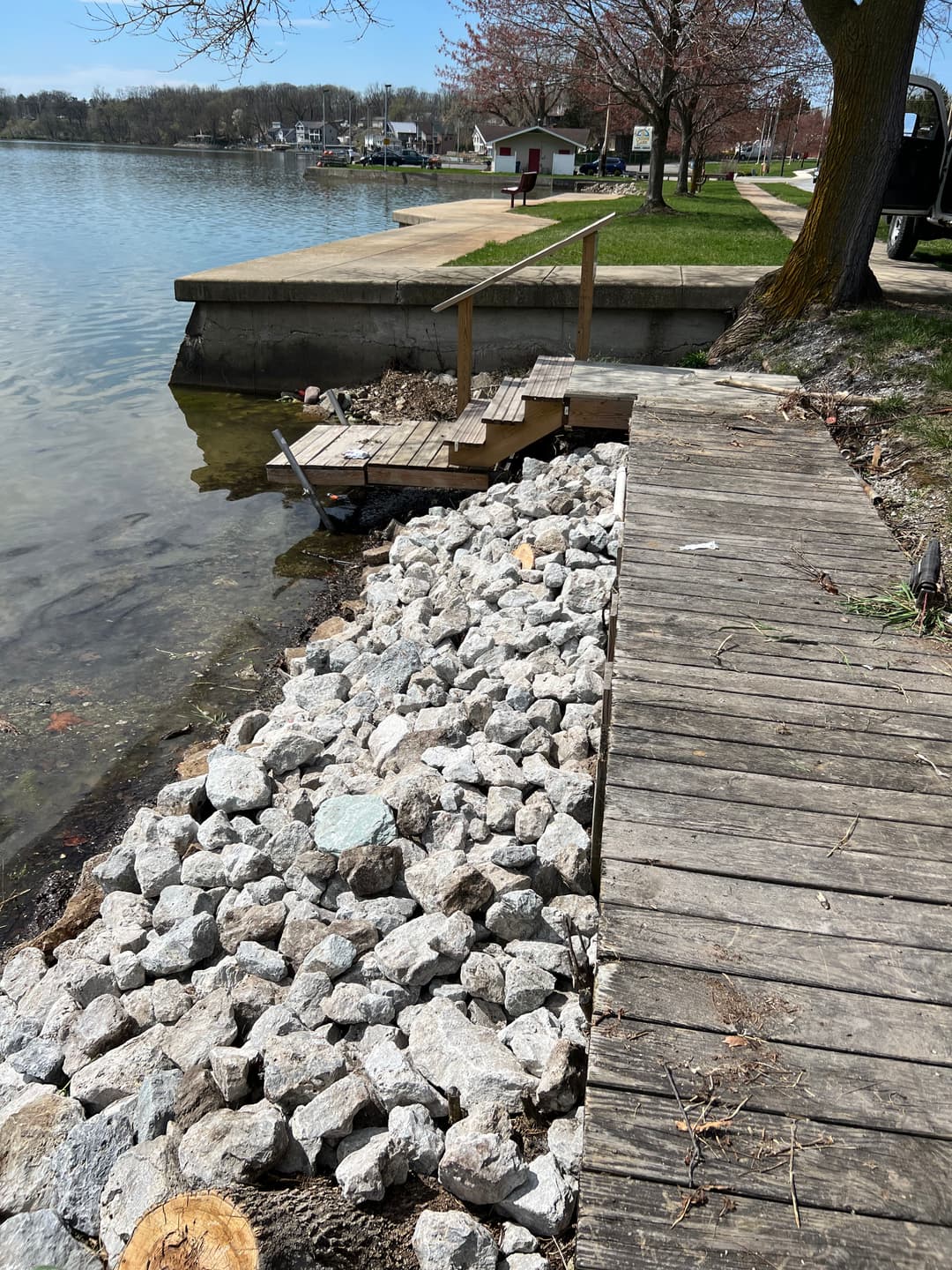 Lakefront dock with wooden walkway and rocky shoreline under clear blue sky. Trees line the shore.