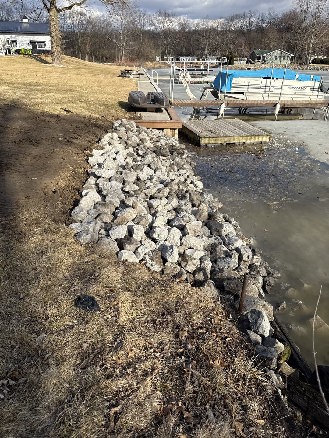 Rocky shoreline with dock and boats at a calm lake on a sunny day.
