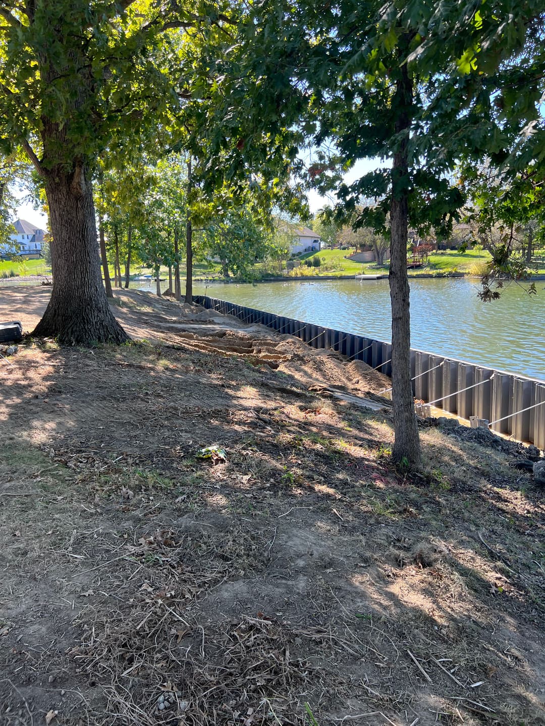 Lakeside property with trees, new retaining wall, and water, enhancing outdoor landscape.