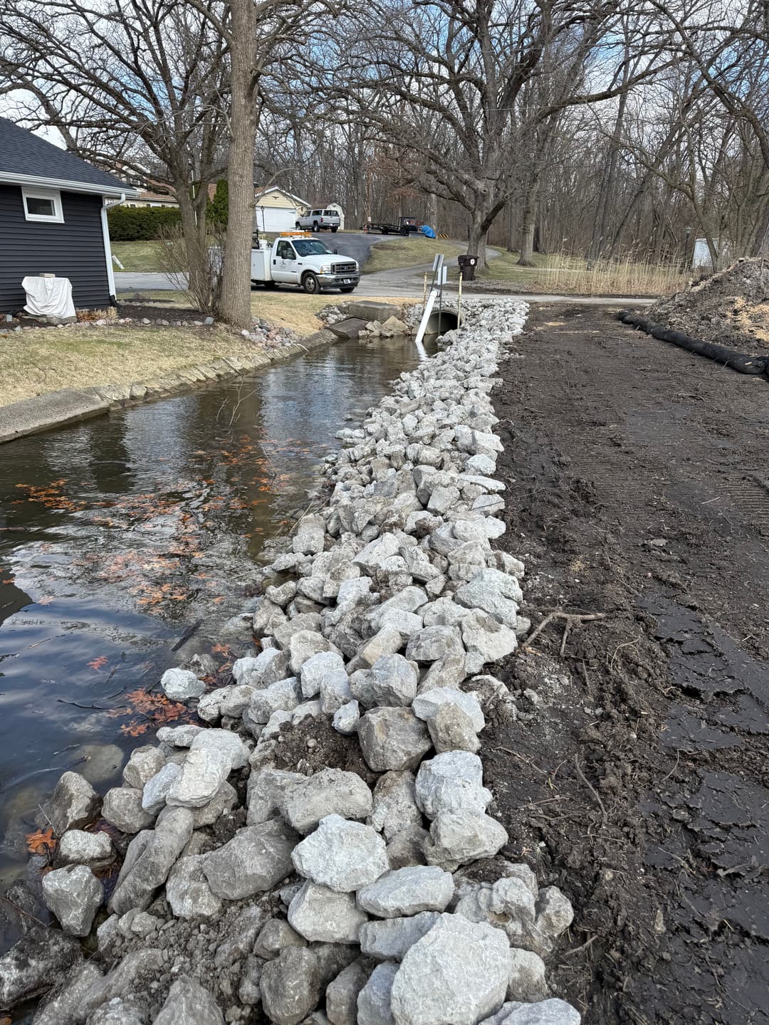 Rock-filled shoreline erosion control structure along a calm waterway near residential area.