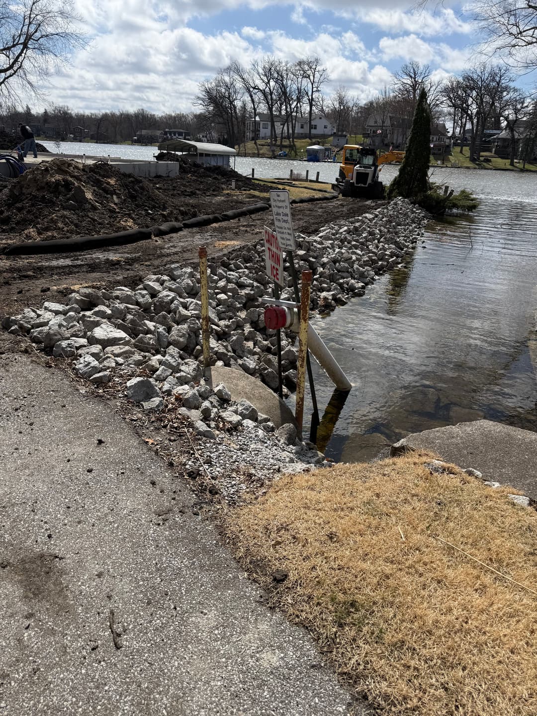 Construction site with rocks and sign near water body, indicating restricted access.