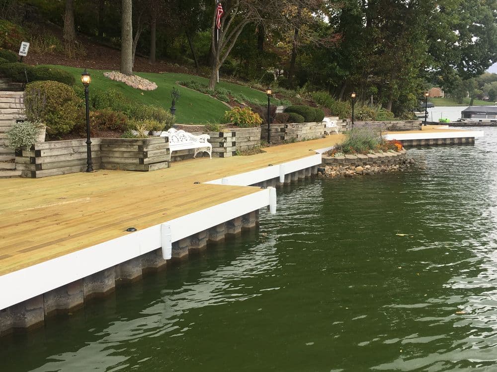 Dock by the water with wooden walkways, benches, and landscaped surroundings.