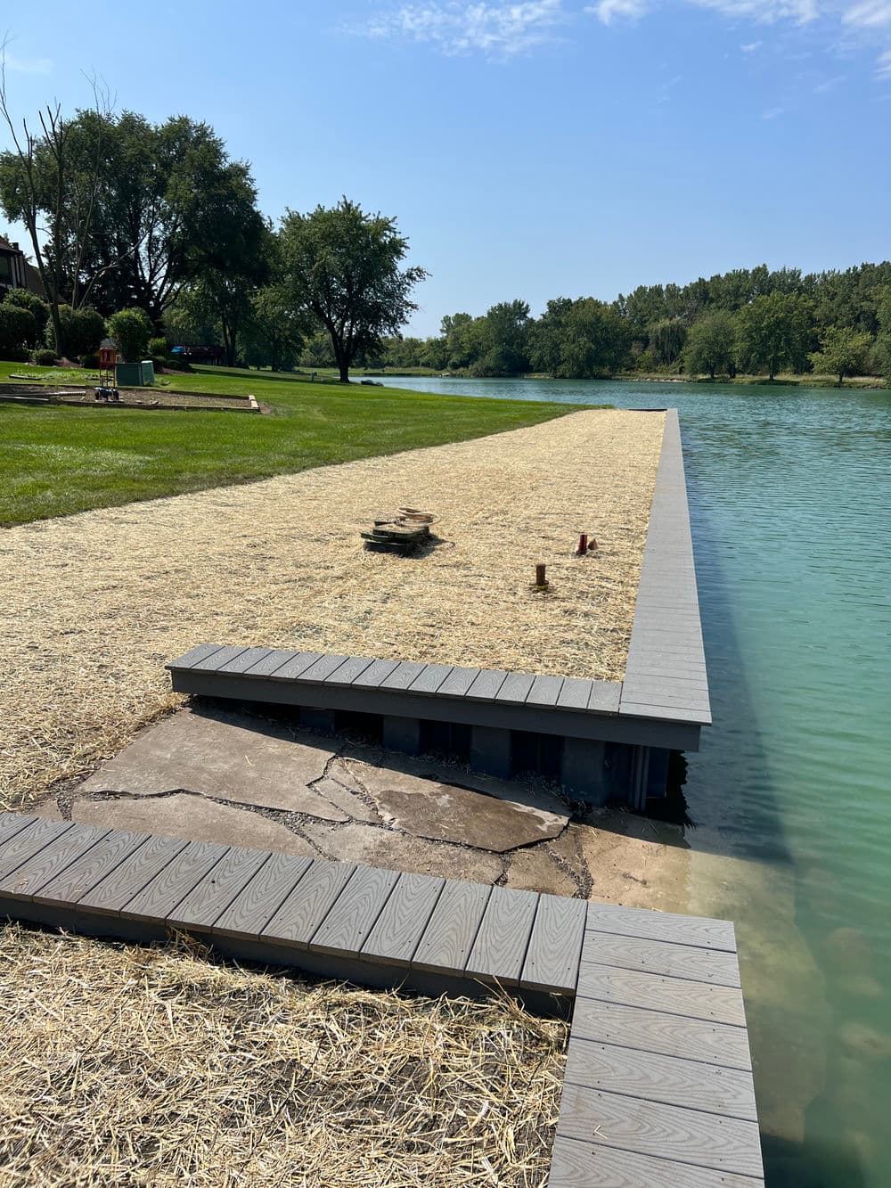 Dock extending into a serene lake with green grass and trees in the background.