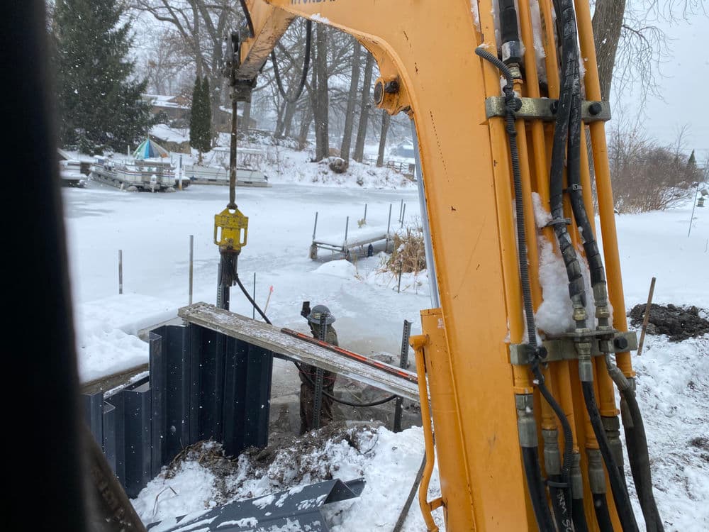 Excavator working on a snowy landscape near a frozen waterway, construction in progress.