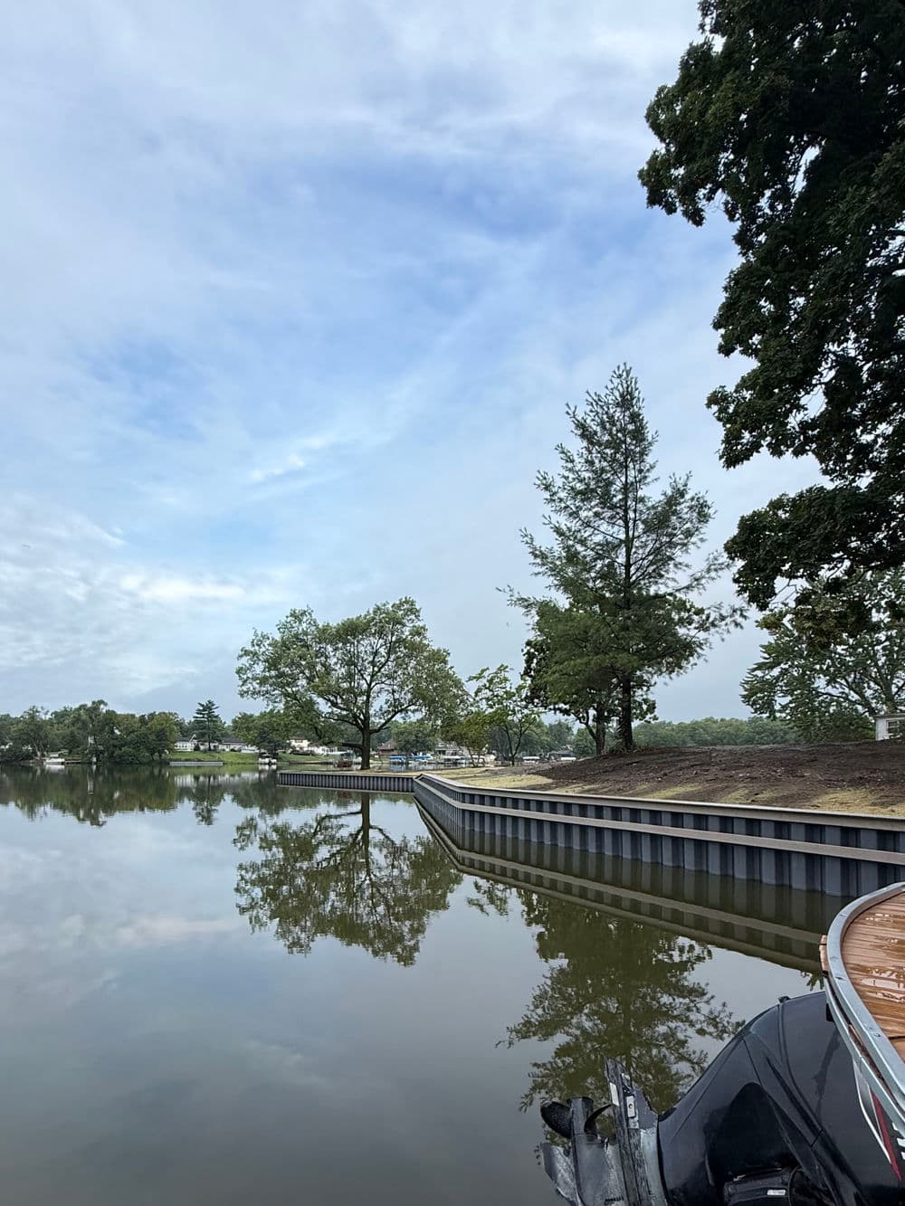 calm lake scene with trees reflecting on water, boat in foreground, cloudy sky
