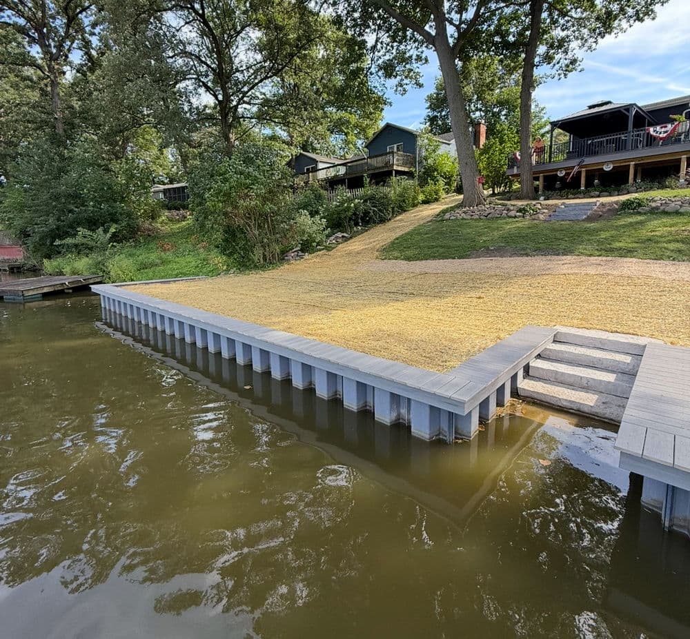 Lakeside dock with wooden steps and homes in the background on a sunny day.