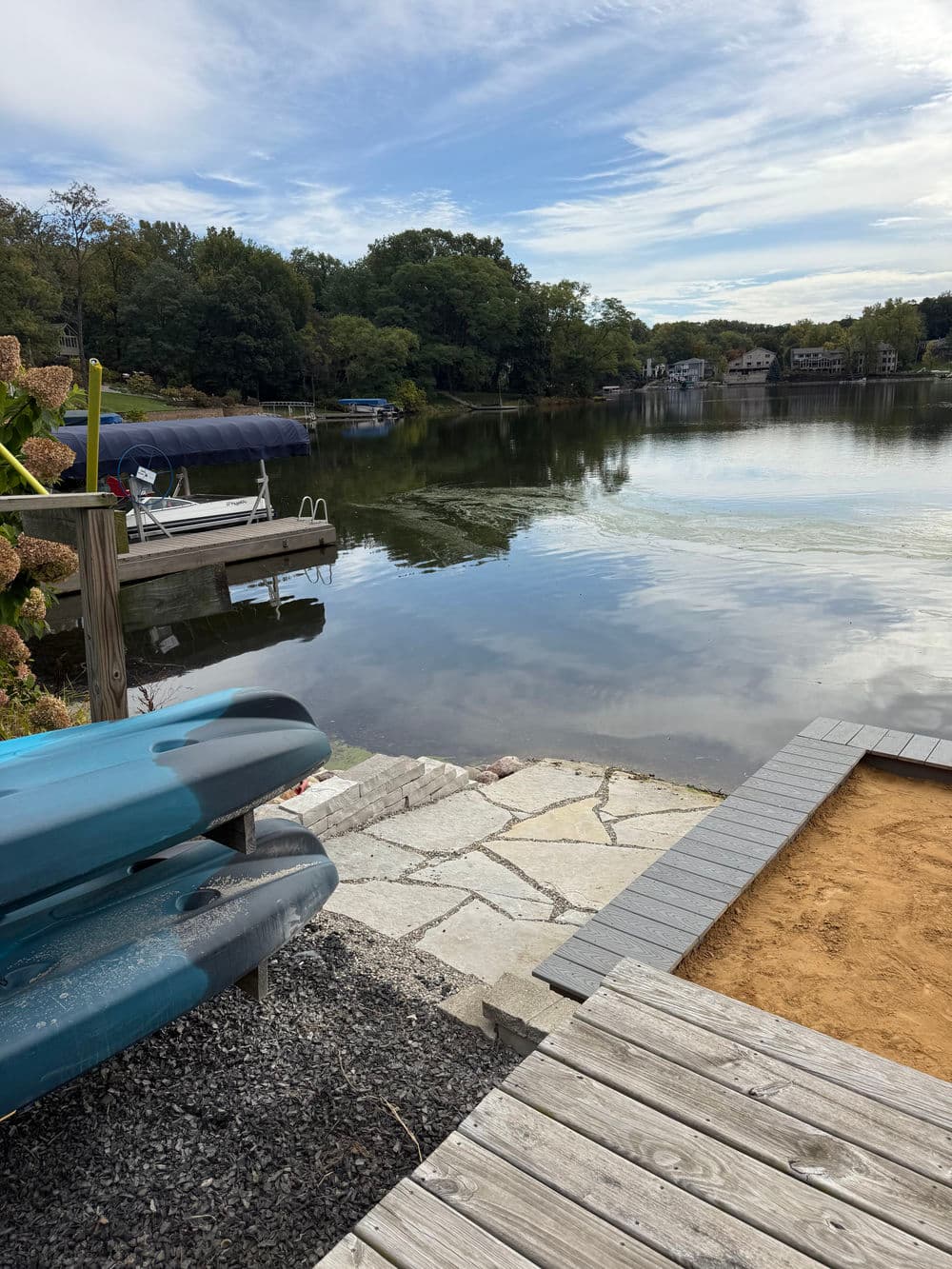 Kayaks by a serene lake with reflections, surrounded by greenery and a dock.